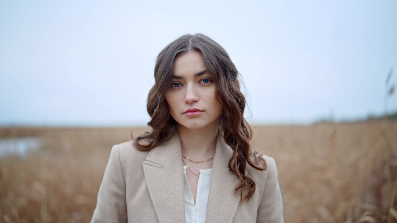 A woman in a camel coat standing in a field of dry reeds